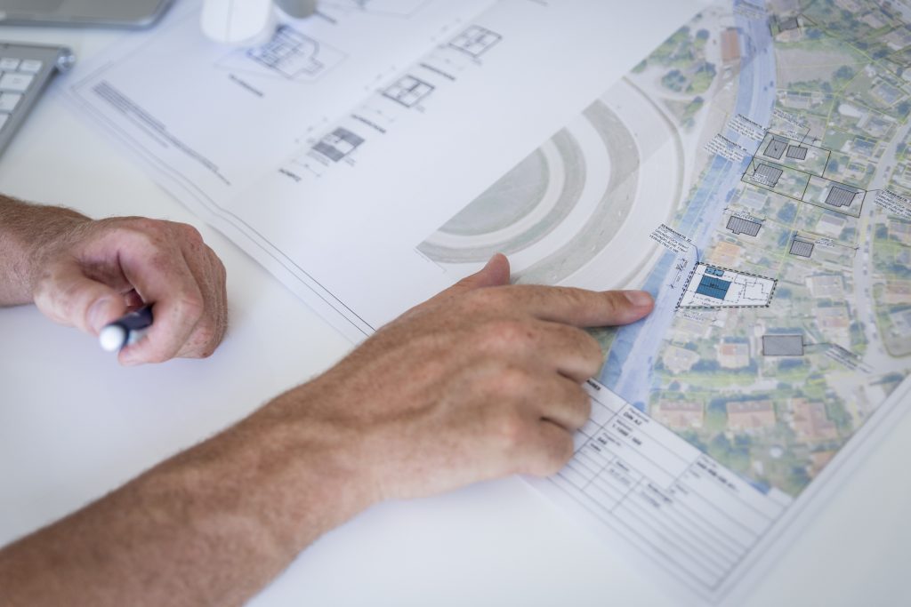 Eine Person die auf eine Karte zeigt auf dem Häuser und Skizzen von Häuser zu sehen sind.
